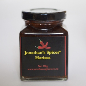 A square shaped glass jar with a black, red and yellow label containing Jonathan's Spices harissa